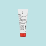 White tube with a red cap on a light blue background, displaying detailed black text on its back label, likely indicating ingredients and usage instructions.
