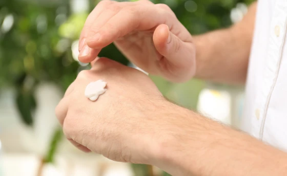 A close up of a person's hands, applying cream on the dorsal of the left hand.