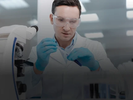 A scientist working in a lab, next to a microscope.